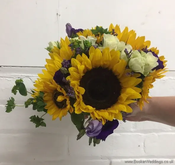 Bridesmaid handtied bouquet with sunflowers, yellow gerberas, white spray roses, purple limoneum and purple lissianthus tilted view